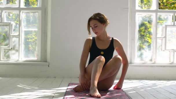 Молода рудоволоса здорова біла біла жінка практикує йогу на килимку у білій великій кімнаті. Молода жінка в спортивному одязі займається фітнесом в приміщенні . — стокове відео
