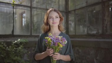 Eski binada duran yabani çiçekleri koklayan genç ve güzel bir kadının portresi. Yaz saati kavramı, dinlenme günü