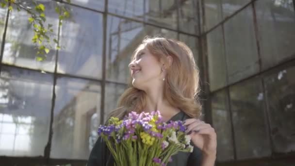 Ritratto di una bella giovane donna con il bouquet di fiori selvatici in piedi presso il vecchio edificio. Concetto di estate, femminilità, giorno di riposo. Serie persone reali . — Video Stock