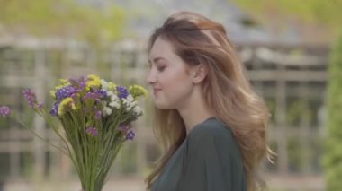 Açık havada poz veren yabani çiçekler buket tutan dalgalı saçlı güzel bir genç kadının portresi. Kadınlık kavramı, bahar ruh hali, kaygısız yaşam. Gerçek insanlar serisi.