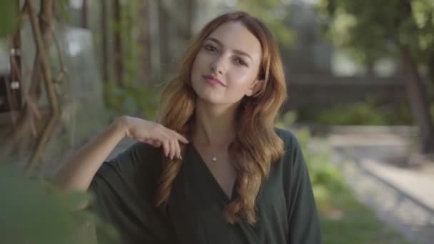 Retrato de una hermosa joven feliz mirando a la cámara y sonriendo mientras estaba de pie en el parque de verano. Concepto de verano, feminidad, día de descanso. Serie de personas reales . — Vídeo de stock