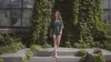 Kendine güvenen güzel genç kadın gülümseyerek kameraya doğru yürüyor ve sonra yeşil yazlık parkta göz kırıyor. Yaz, kadınlık, dinlenme günü kavramı