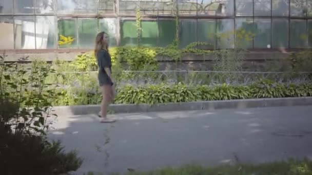 Eine selbstbewusste junge Frau geht am alten Gebäude vorbei und hält einen Strauß wilder Blumen in der Hand. Konzept der Sommerzeit, Weiblichkeit, Ruhetag. ländlicher Lebensstil — Stockvideo