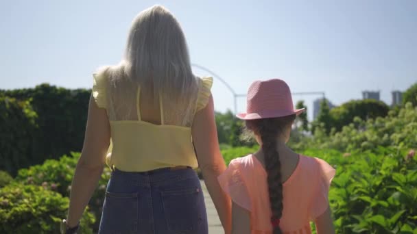 Widok z tyłu blond matka chodzenie z córką w ogrodzie letnim trzymając ręce. Szczęśliwa rodzina, jeden rodzic. Połączenie z naturą. Życie na wsi — Wideo stockowe