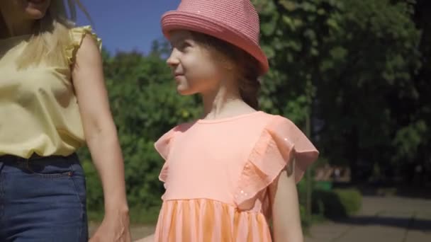 Linda madre rubia caminando con una pequeña hija adorable en el jardín de verano cogida de la mano. Familia feliz. Mujer y chica juntas al aire libre . — Vídeos de Stock