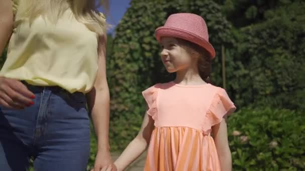 Madre caminando con una pequeña y adorable hija en el jardín de verano cogida de la mano. Familia feliz. Mujer y chica juntas al aire libre . — Vídeos de Stock