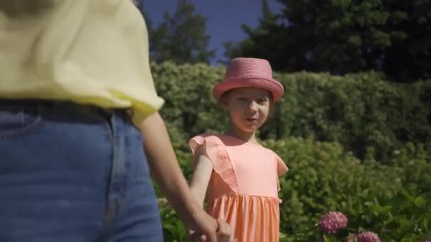 Unerkannte Mutter, die mit kleiner entzückender Tochter Händchen haltend im Sommergarten spaziert. glückliche Familie. Frau und Mädchen zusammen im Freien. — Stockvideo