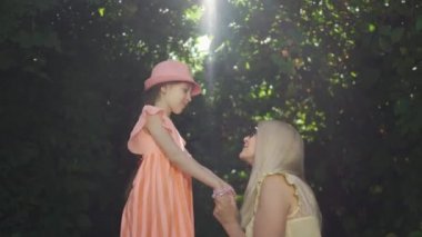 Güzel anne ve kızı yaz bahçesinde ya da parkta birlikte vakit geçiriyorlar. Kızın ellerini öpen kadın, annesini öpen kız. Mutlu bir aile. Kadın ve küçük kız birlikte açık havada.