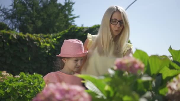 Блондинка в окулярах навчає доньку доглядати за садом. Щаслива сім'я, один батько. Зв'язок з природою. Сільське життя. Жінка і дівчина разом на відкритому повітрі . — стокове відео