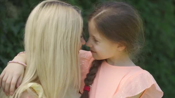 Portret van moeder zoenen haar kleine dochter. Schattige blonde moeder en haar kleine dochter knuffelen in het zomerpark. Gelukkig liefdevolle familie. Vrouw en meisje samen buitenshuis. — Stockvideo