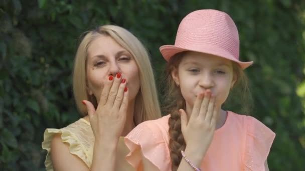 Close-up portrait of blond mother and her little daughter sending air kiss looking at the camera while sitting in the summer park. Happy loving family. Woman and girl together outdoors. — Stock Video