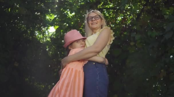 De vrouw en het meisje knuffelen. Rijpe blonde moeder en haar dochter tijd samen doorbrengen in de zomertuin of Park kijken naar camera. Gelukkige familie. Vrouw en meisje buitenshuis. — Stockvideo