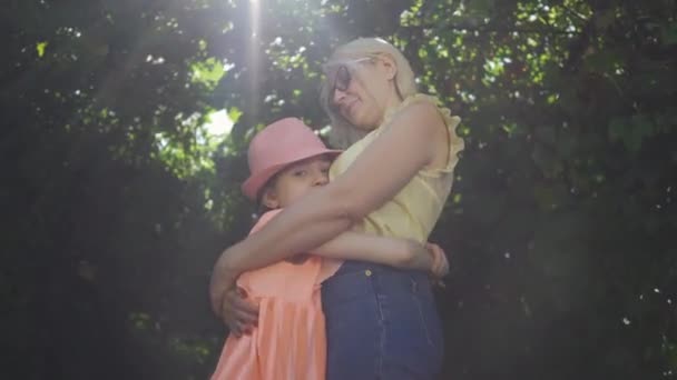 Blond moeder en haar dochter tijd doorbrengen samen in de zomertuin of Park. De vrouw en het meisje knuffelen. Gelukkige familie. Vrouw en meisje buitenshuis. — Stockvideo