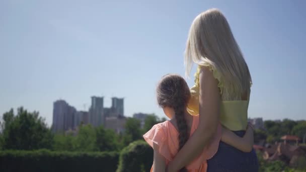 Lazer de mãe loira e sua filha pequena no jardim ou parque de verão. A rapariga a abraçar a mãe. Família feliz. Mulher e menina juntos ao ar livre . — Vídeo de Stock