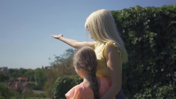 La madre rubia y su hijita pasan tiempo juntas en el parque de verano. La mujer y la muchacha que admiran el paisaje hermoso. Familia feliz . — Vídeos de Stock