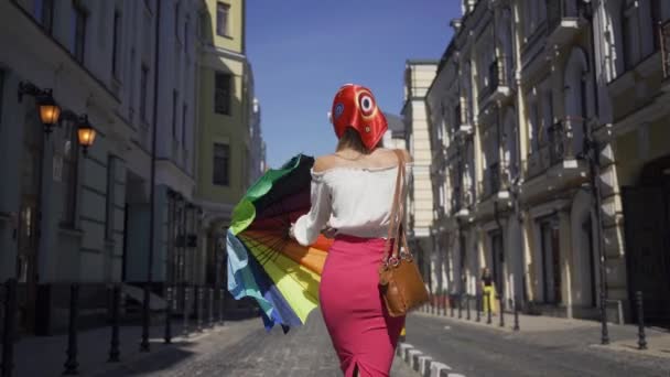 Mulher bonita positivo andando na rua, girando e olhando para a câmera segurando guarda-chuva multicolorido. Menina elegante atraente desfrutando de dia ensolarado na cidade europeia velha — Vídeo de Stock