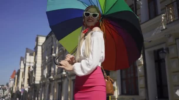 Pretty ung kvinna tittar på kameran håller mångfärgade paraply stående på gatan. Attraktiv fashionabla flicka njuter solig dag i den gamla europeiska staden. Turism koncept. — Stockvideo