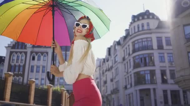 Retrato joven mujer divertida mirando a la cámara sosteniendo paraguas multicolor de pie en la calle. Atractiva chica de moda disfrutando de un día soleado en la vieja ciudad europea. Concepto turístico . — Vídeo de stock