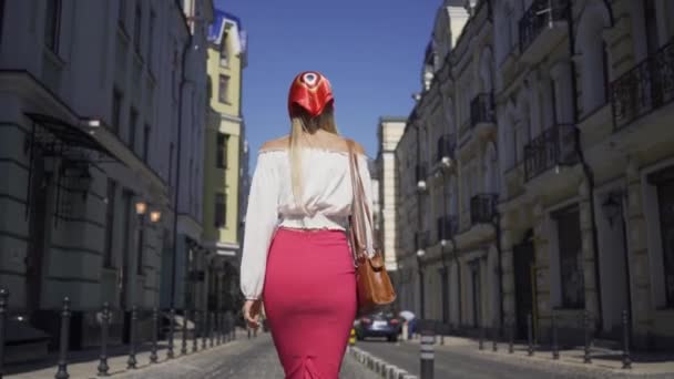 Обратный вид на красивую молодую женщину, идущую по улице, поворачивающуюся и смотрящую в камеру, делающую привлекательный жест. Привлекательная модная девушка наслаждается солнечным днем в старом европейском городе — стоковое видео