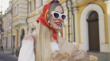 Sevimli genç kadın taze pişmiş ekmek ve kruvasan tutan sokakta duruyor. Eski Avrupa şehrinde güneşli bir günün tadını çıkaran çekici modaya uygun kız. Turizm konsepti