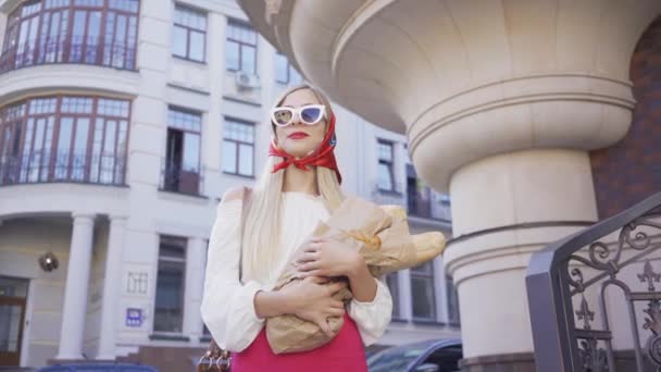 Retrato de uma jovem bonita de pé na rua segurando pão recém-assado e croissant. Menina na moda atraente desfrutando de dia ensolarado na antiga cidade europeia. Conceito de turismo, férias — Vídeo de Stock