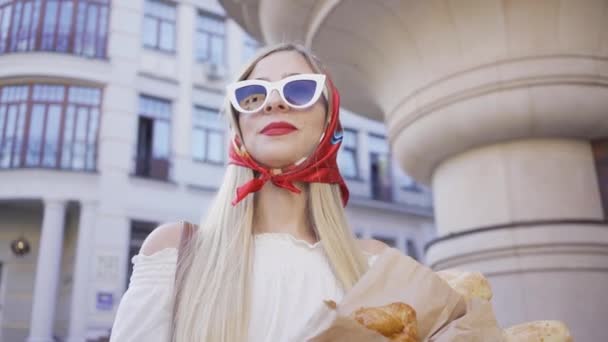 Portret van mode jonge vrouw staande op de straat met vers gebakken brood en croissant. Aantrekkelijke modieuze meisje genieten van zonnige dag in de oude Europese stad. Tourism concept, vakantie — Stockvideo