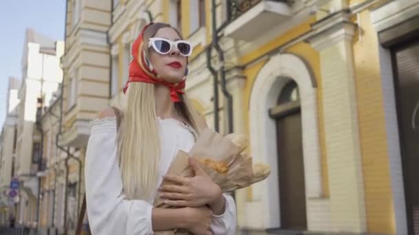 갓 구운 빵과 크루아상을 들고 거리를 걷는 긍정적 인 아름다운 젊은 여성. 오래된 유럽 도시에서 화창한 날을 즐기는 매력적인 유행 소녀. 관광 개념 — 비디오