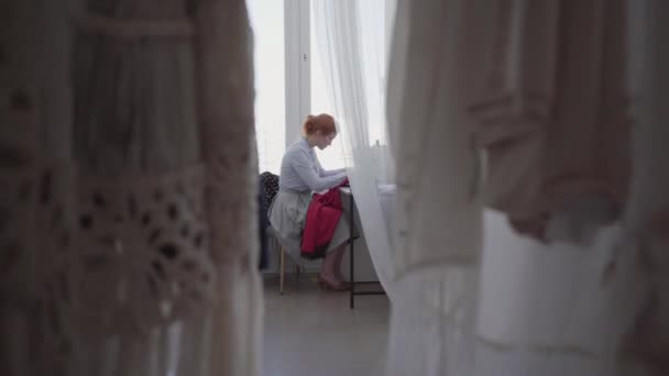 Profesionální rudovlasá žena sejí u stolu v dílně. Švadlena pracuje pilně a pečlivě. Hobby a práci. Šicí oděvy. — Stock video