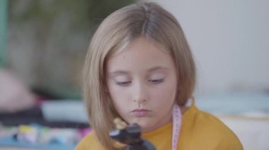 Portre küçük üzgün kızı meşgul annesi arka planda giysi diker ise küçük kukla inceler. Terzi evde çalışıyor. İletişim eksikliği.