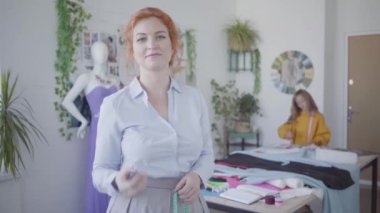Çekici kızıl saçlı terzi portresi kusma ve kamera gülümseyerek izlerken yakalamak ise küçük kızı arka planda çizim. Atölyede birlikte çalışan mutlu aile.