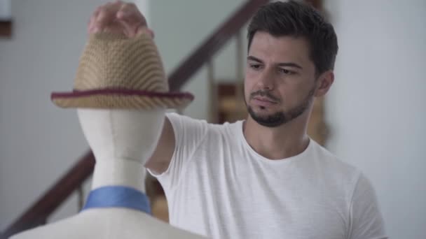 Portrait of young bearded handsome guy taking off his straw summer hat from a mannequin and putting on his head — Stock Video