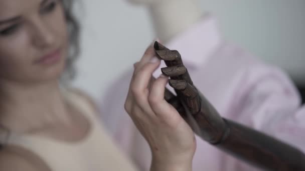 Curly brunette woman touching artificial hand and moving fingers of mannequin in hat and shirt on the background of showroom or shop — Stock Video