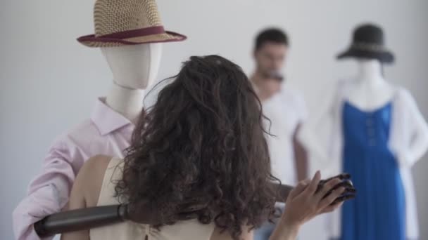 Back view of curly woman dancing with male mannequin in the hat while the man drinking wine in the background. Dreaming concept, imagination, loneliness — Stock Video