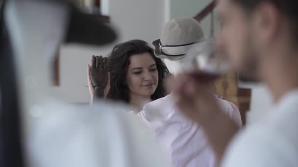 Brunette woman tenderly touching hand of male mannequin in the hat while the man drinking wine in the foreground. Dreaming concept, imagination, loneliness — Stock Video