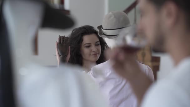 Mujer morena tiernamente tocando la mano del maniquí masculino en el sombrero, mientras que el hombre bebiendo vino en primer plano. Concepto de ensueño, imaginación, soledad — Vídeos de Stock