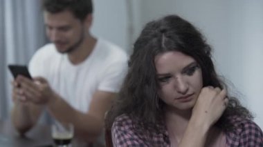 Ağlayan kadın ön planda dönerek ve başka bir kadınla sohbet ederken gülümseyen sadakatsiz kocasına bakıyor. Hile kavramı, kırık aile.