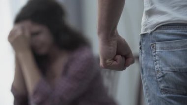 Korkmuş karısının önünde yumruğunu sıkan kızgın bir adamın yakın çekim. Ailede şiddet. Mutsuz bir ilişki. Fiziksel taciz kurbanı. Arka plana odaklanın.