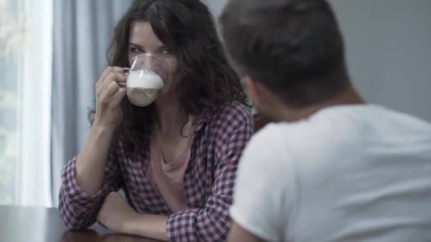 朝、自宅で夫と話しながらコーヒーを飲む幸せな女性の肖像画。幸せな家族は家で休んでいます。友好的な関係。肩越しに撮影 — ストック動画