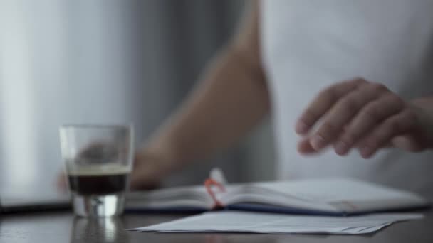 Gros plan de l'homme en t-shirt blanc travaillant avec des papiers et buvant du café à la maison ou au bureau. Le gars qui étudie ou travaille à l'intérieur. Concept freelance — Video