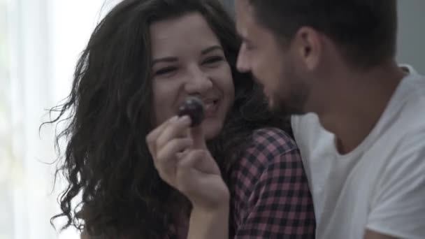 Retrato de una mujer feliz alimentando a su marido con jugosa ciruela sentada en casa por la mañana. Familia feliz descansando en casa. Relación amistosa — Vídeo de stock