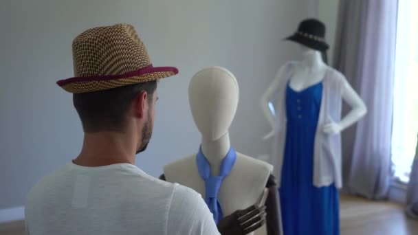 Vista trasera de un joven poniendo su sombrero en la cabeza del maniquí. El tipo que se divierte en el estudio de costura o tienda de ropa — Vídeo de stock