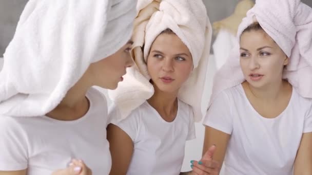 Retrato de tres lindas novias en camisetas blancas con toallas en las cabezas charlando en casa en el baño. Fiesta de gallinas, fiesta de pijamas. Las niñas se divierten en interiores — Vídeos de Stock