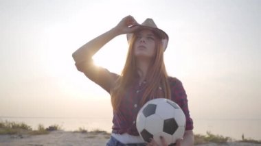 Genç güzel kız Portresi dinlenmek ve eğlenmek için yaz akşamı futbol topu ile plaja geldi