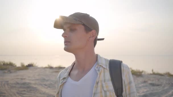 해안선 근처 화창한 저녁 해변에서 피크닉을위한 친구와 장소를 찾는 젊은 매력적인 남자의 초상화 — 비디오