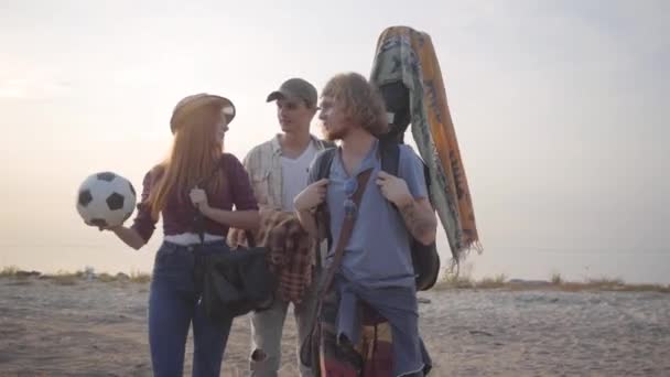 Drie jonge vrienden kwamen naar het strand met gitaar en voetbal bal op de zomeravond om te ontspannen en plezier te hebben — Stockvideo