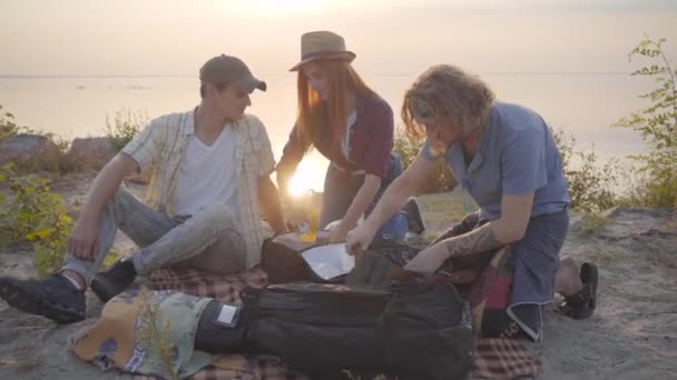 Grupo de jóvenes amigos haciendo picnic con guitarra y chica sacaron de la bolsa cerveza fría o limonada — Vídeo de stock