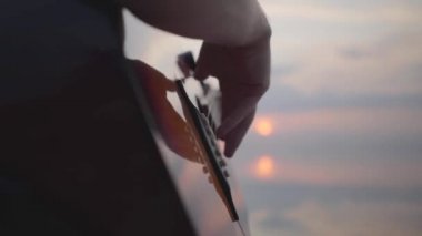 Yaz plajı yakınında akşam renkli gün batımı arka planda gitar çalan erkek el yakın çekim.