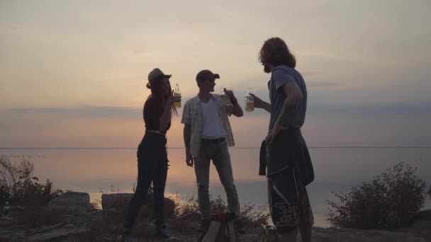Grupo de jóvenes amigos charlando con cerveza fría o limonada relajándose y divirtiéndose con buen humor en el fondo de la impresionante puesta de sol — Vídeo de stock