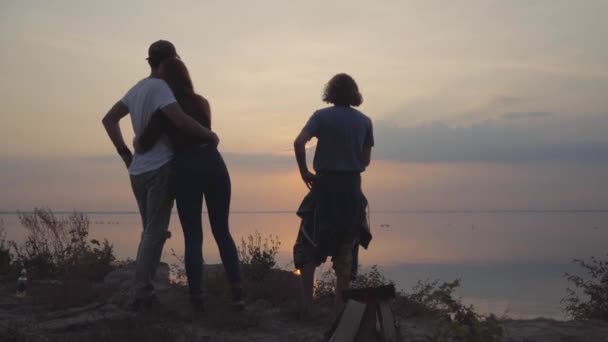 Grupo de jóvenes amigos relajándose con cerveza fría o limonada charlando, abrazando y divirtiéndose con buen humor en el fondo de la impresionante puesta de sol — Vídeo de stock