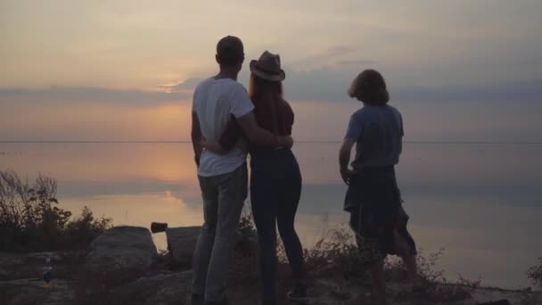 Grupo de amigos relajándose con cerveza fría o limonada charlando, abrazando y divirtiéndose con buen humor en el fondo de la impresionante puesta de sol — Vídeos de Stock